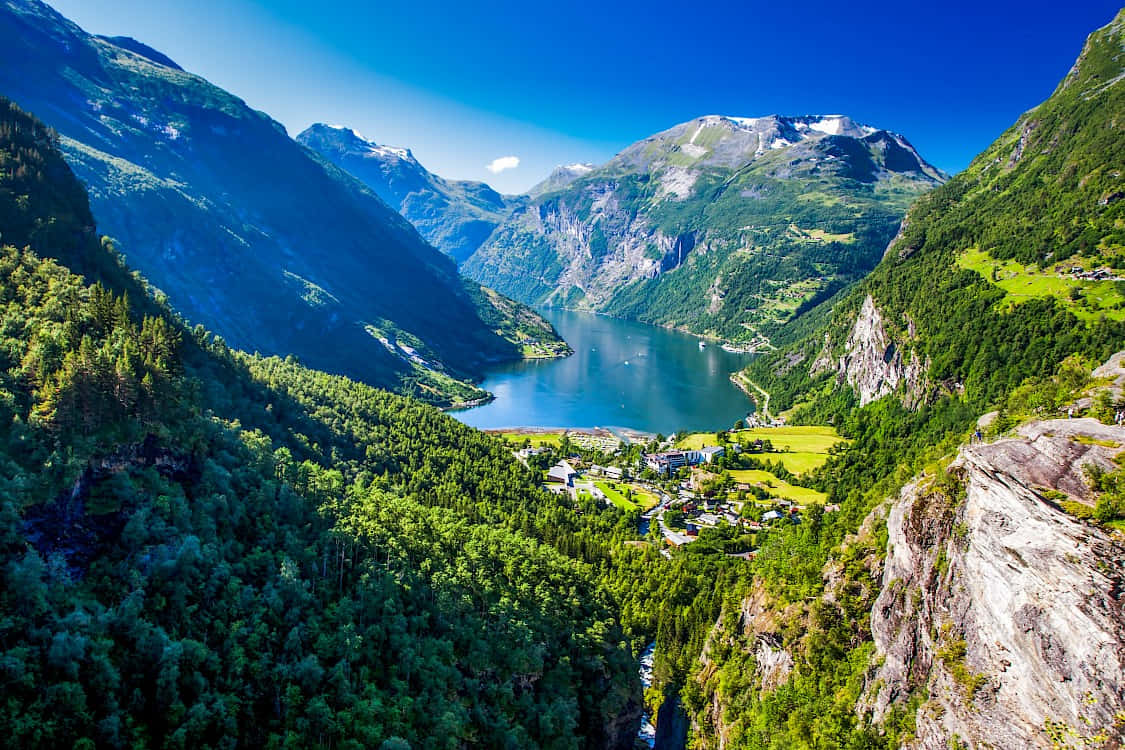  壁紙 — 從高空俯瞰，寧靜的峽灣坐落於高聳的翠綠山巒之間，上方是清澈的藍天。