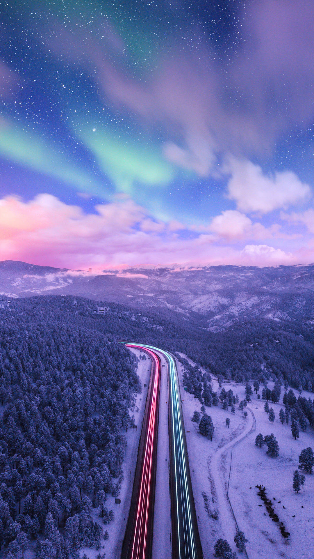 白雪覆蓋的山區高速公路，在舞動的北極光下閃爍著光跡。 — Google 壁紙