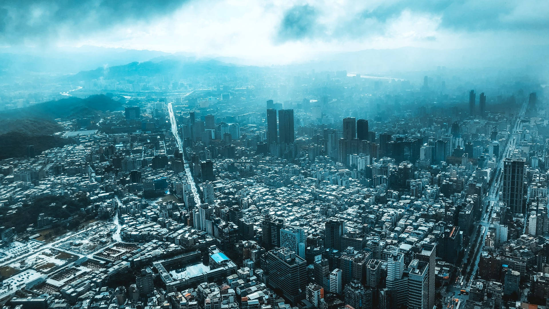 在多雲的天空下，以摩天大樓和山脈為背景的密集城市的鳥瞰圖。 — 台北 壁紙