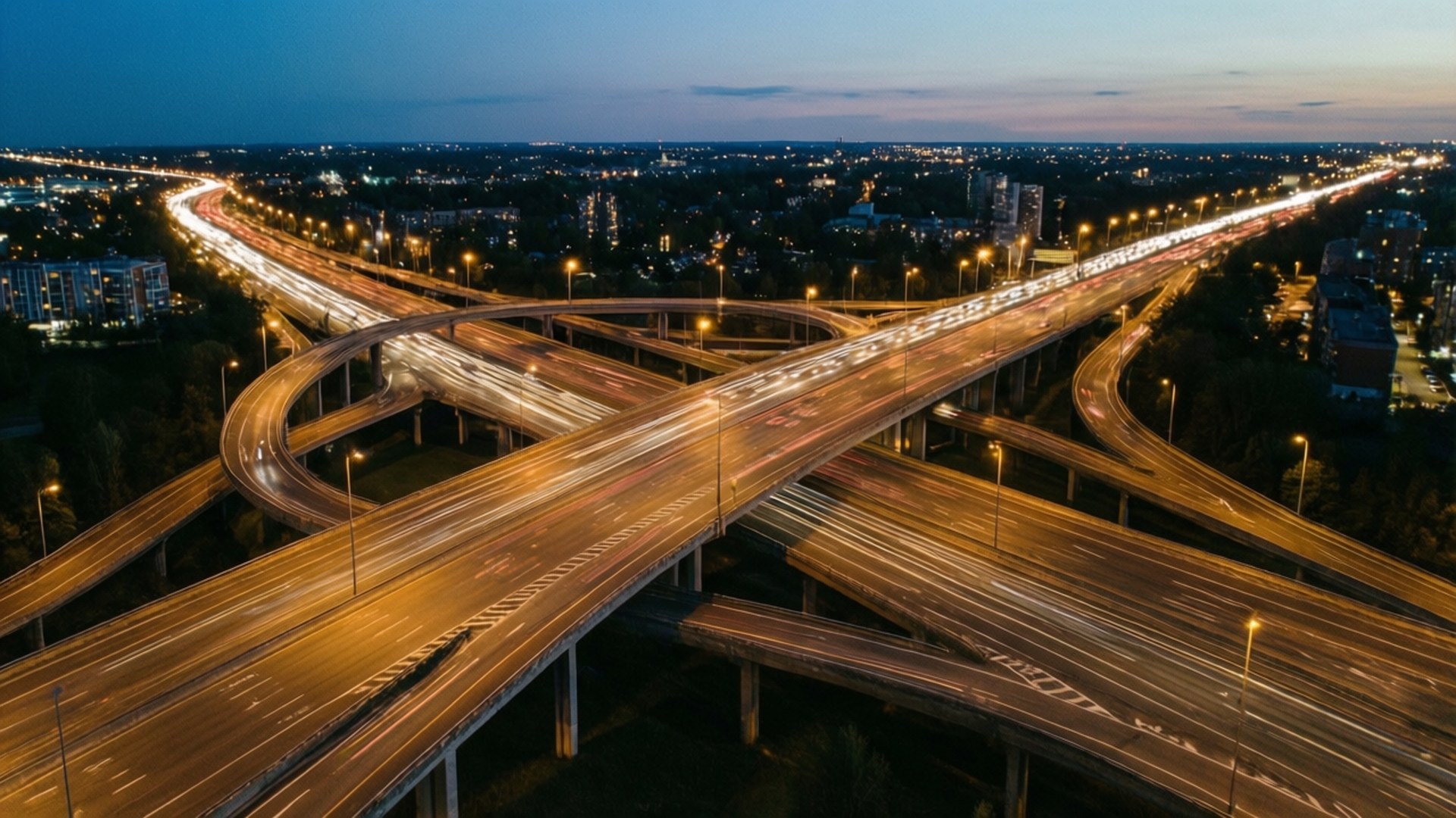 City Interchange 壁紙 — 黃昏時分廣闊高速公路交匯處的鳥瞰圖，移動車輛發出閃爍的光跡。