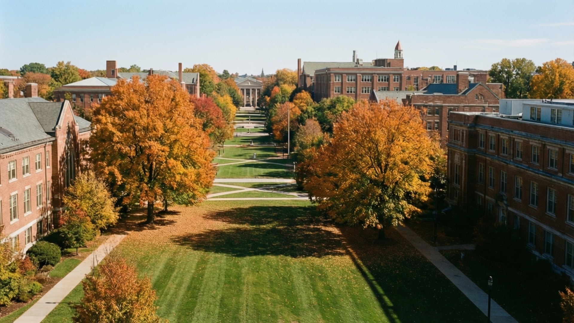 Autumn Campus 壁紙 — 秋季大學校園的鳥瞰圖，鮮豔的橙色樹木排列在綠色草坪和磚砌建築旁，天空清澈湛藍。