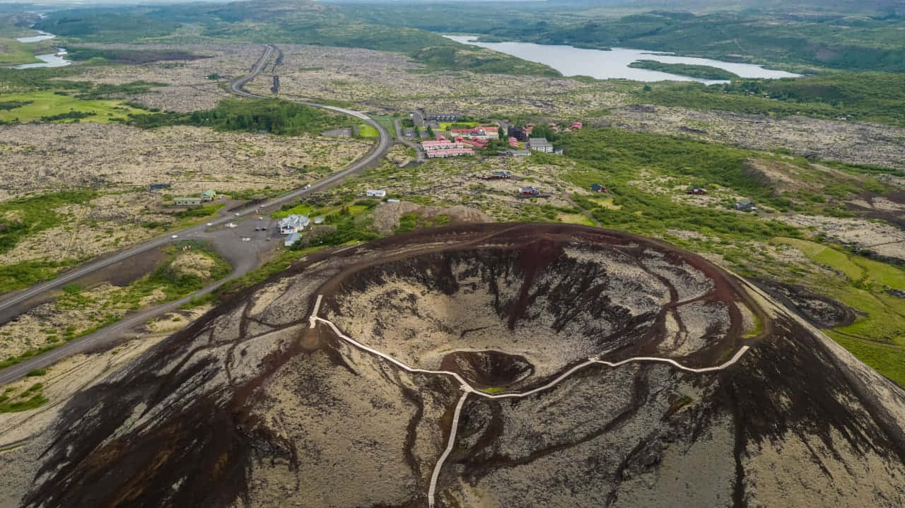  壁紙 — 晴朗天空下，火山口俯瞰圖，蜿蜒小徑被綠色田野和遠處湖泊環繞。