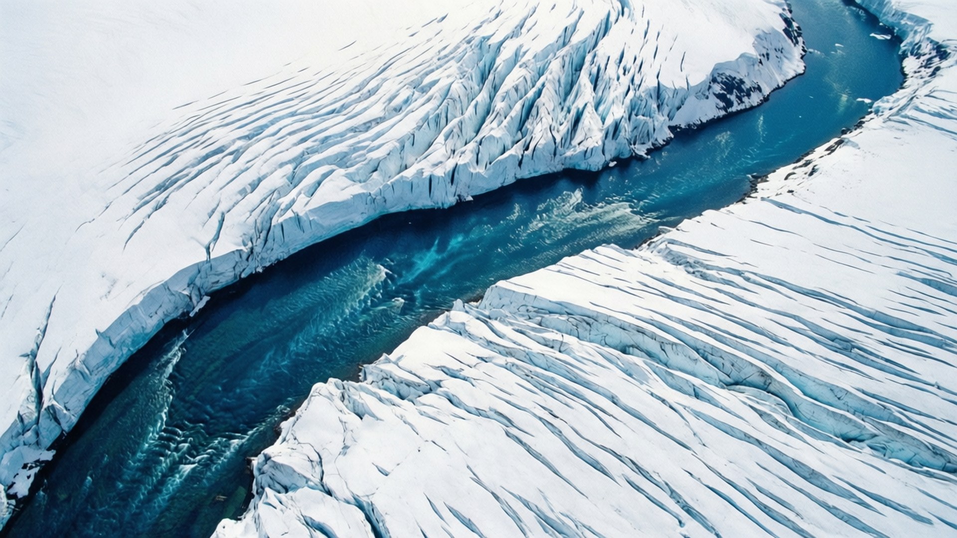 Glacier River Aerial 壁紙 — 從空中俯瞰，一條蜿蜒的藍綠色冰川河流穿過紋理分明的白雪和冰層。