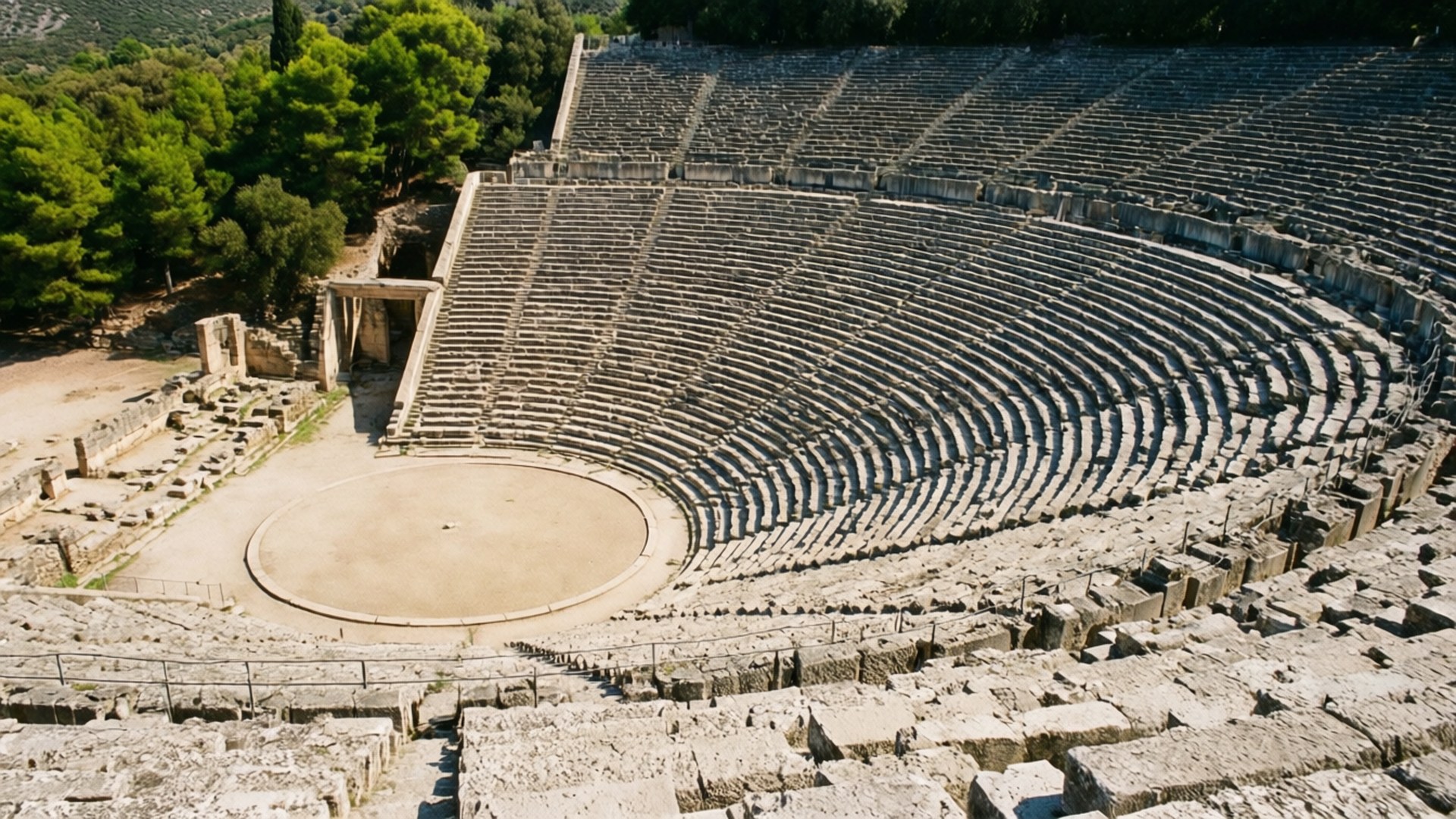 Epidaurus Amphitheater 壁紙 — 俯瞰古老石造圓形劇場，彎曲的階梯式座位環繞著圓形舞台，坐落於綠樹成蔭的山坡上。
