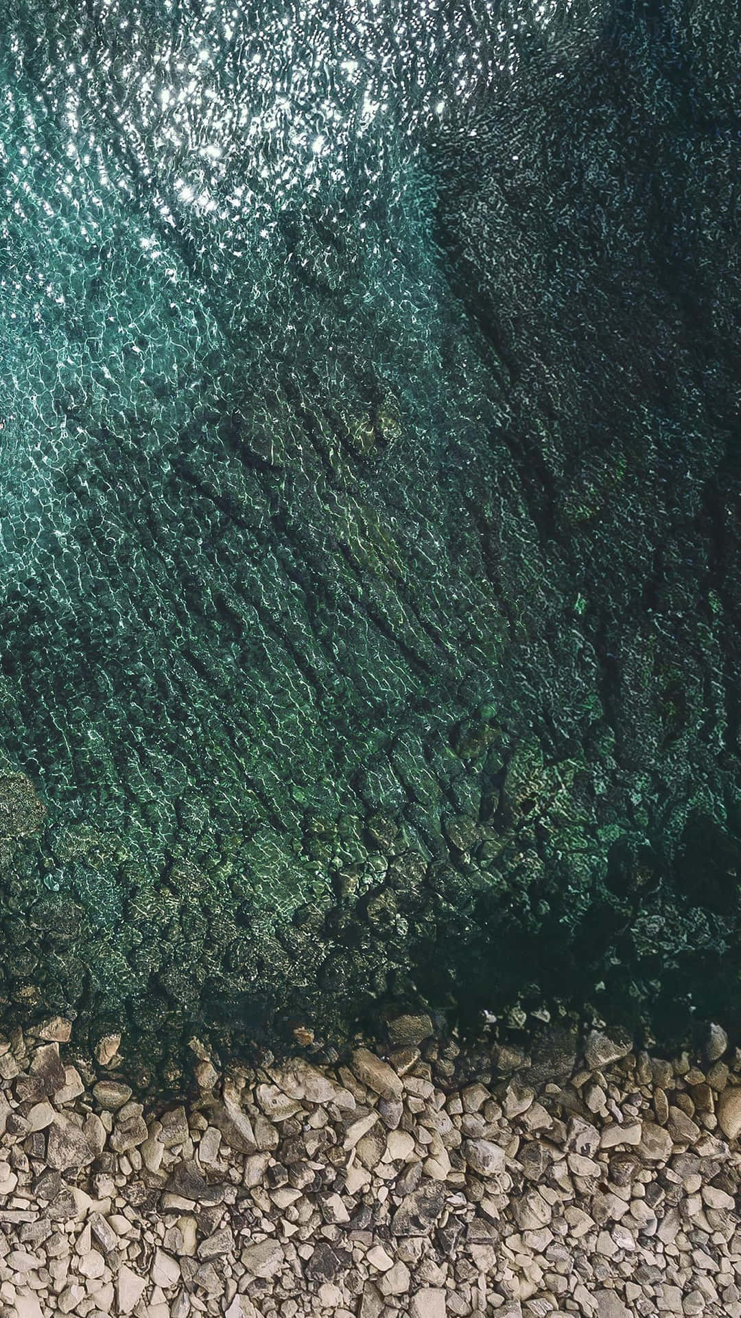 平靜海岸線上，清澈碧綠的海水在陽光照射的岩石上泛起漣漪。 — iPad 壁紙