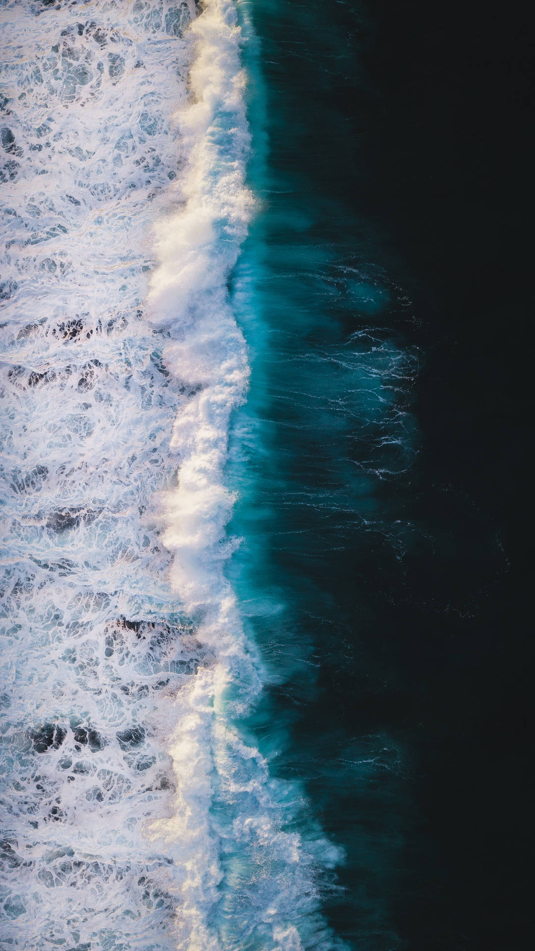 從高空拍攝海洋波浪在深藍色海水中破碎成白色泡沫。 — Oled 壁紙