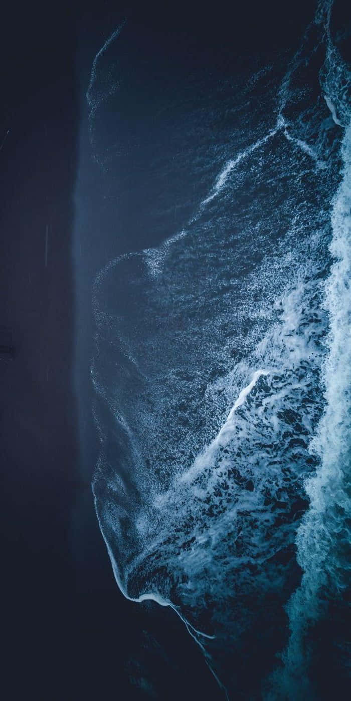  壁紙 — 黃昏時分深藍色海浪拍打深色沙灘的航拍視圖。