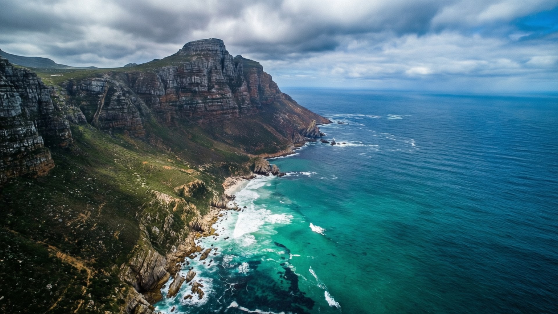Cape of Good Hope Aerial 壁紙 — 多雲天空下，戲劇性懸崖與碧綠海洋交匯的鳥瞰圖。