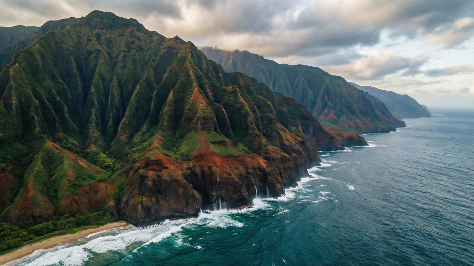Na Pali Coast Drama 壁紙 — 從空中俯瞰戲劇性的綠色和紅色懸崖，直插入綠松石色的海洋，白色波浪拍打岩石海岸，天空多雲。