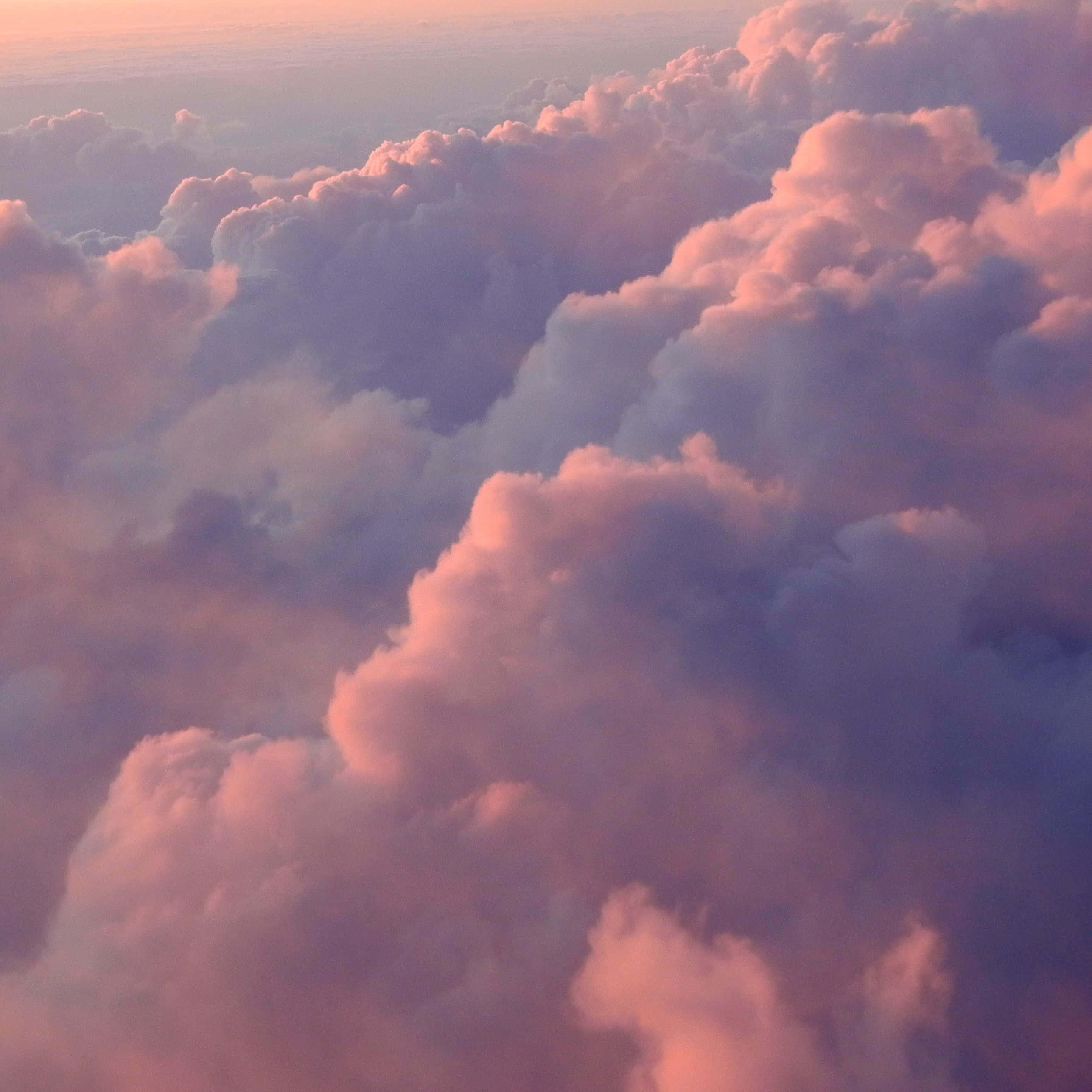 Cloud Aesthetic 桌布 壁紙 — 日出或日落時，蓬鬆雲朵沐浴在柔和粉紅與紫色調中的鳥瞰圖。