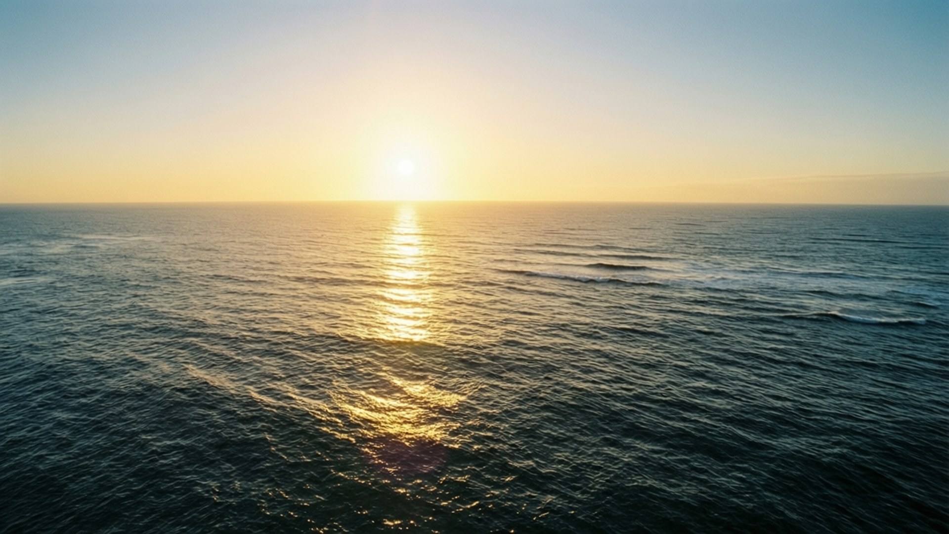 Golden Ocean Sunrise 壁紙 — 晴朗藍天下，金色日出映照在平靜海浪上的鳥瞰圖。