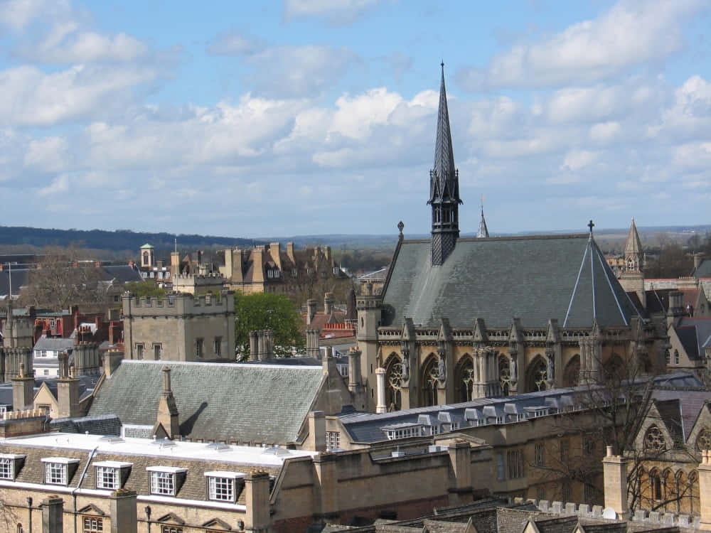 Oxford United Kingdom 桌布 壁紙 — 歷史石砌建築的鳥瞰圖，一座突出的哥德式教堂尖塔刺穿部分多雲的藍天。