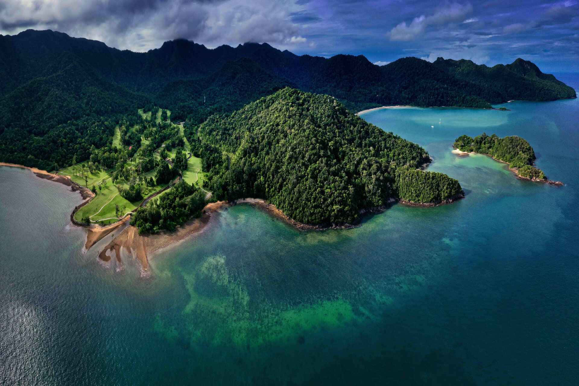  壁紙 — 俯瞰鬱鬱蔥蔥的綠色島嶼，碧綠海水和高爾夫球場隱藏在茂密的叢林中。