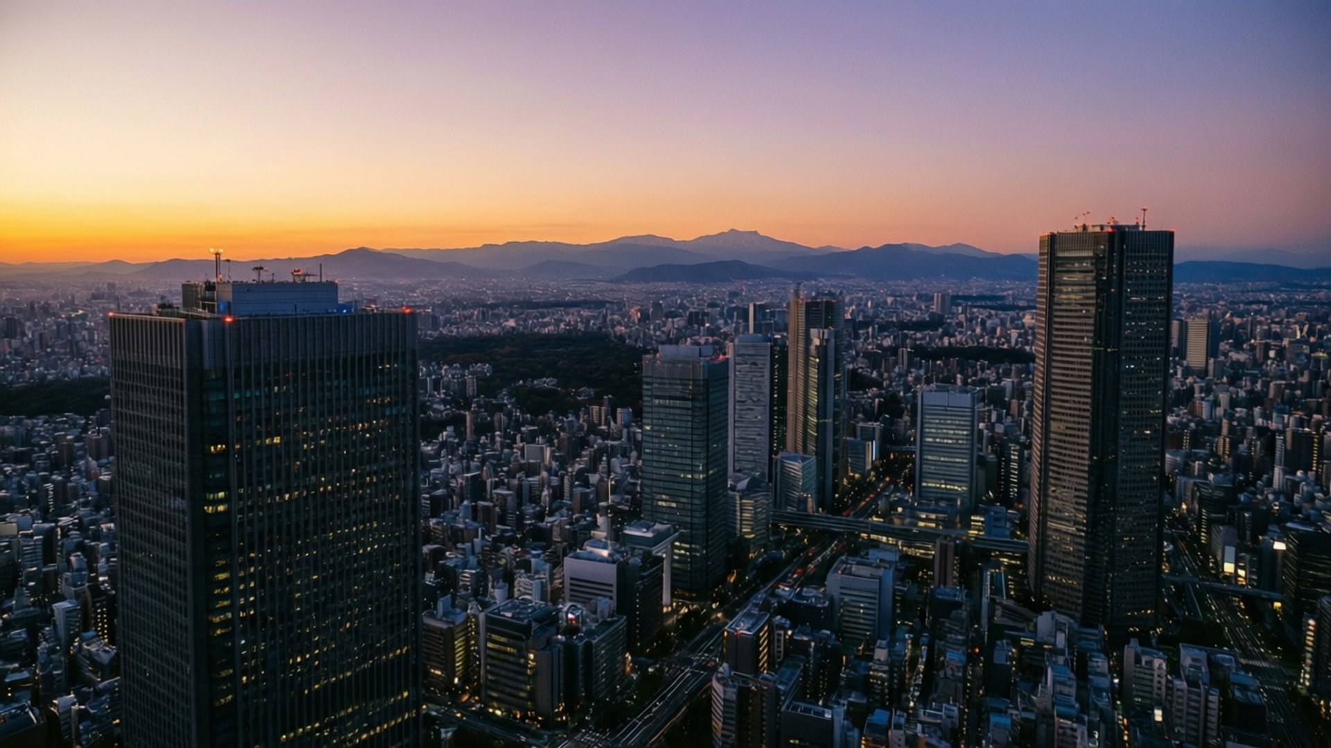 Cityscape from Abeno Harukas 壁紙 — 黃昏時分東京天際線的鳥瞰圖，在漸變的紫橙色天空下，有燈火通明的摩天大樓和遠山。