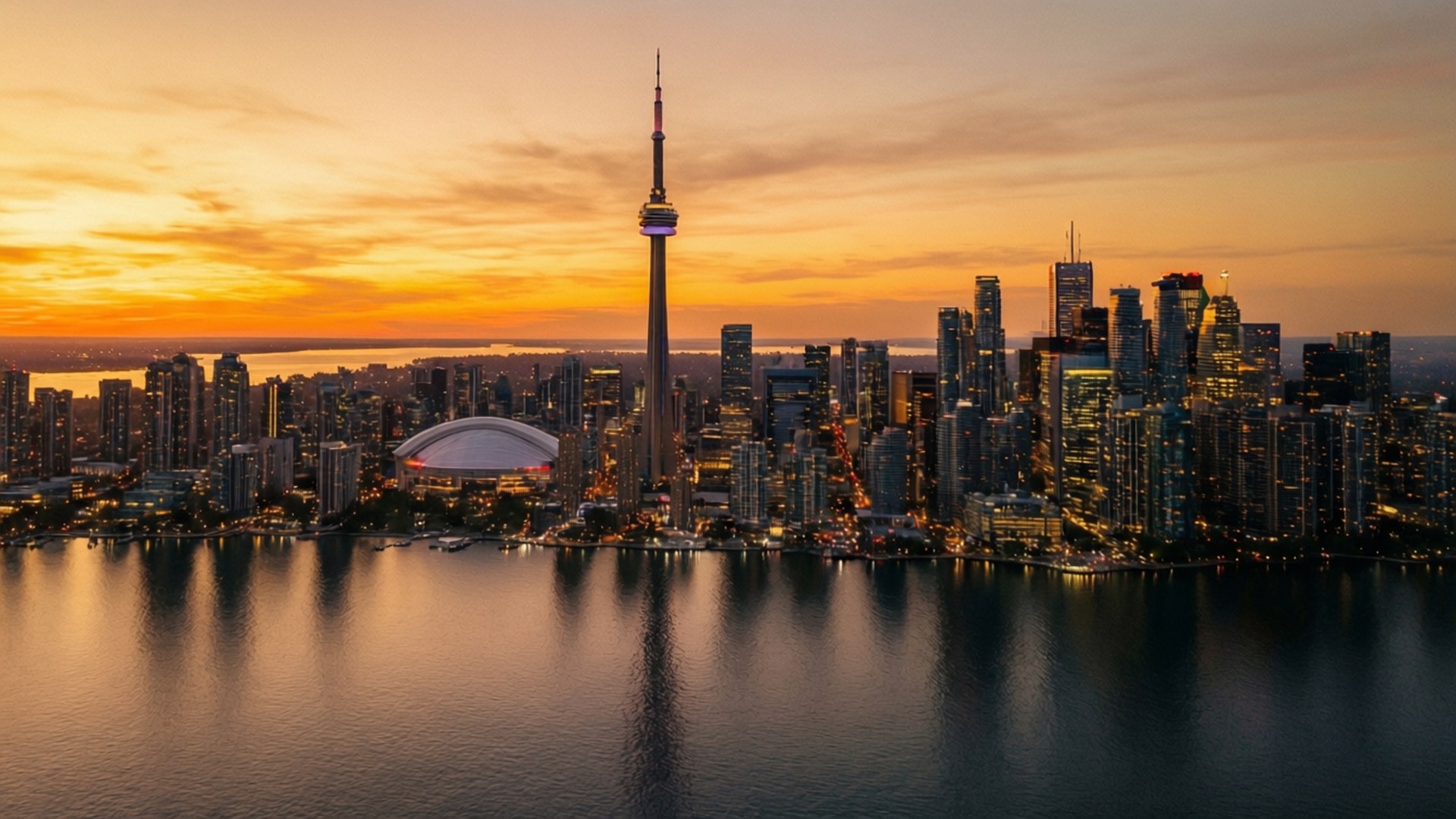 Toronto Sunset Skyline 壁紙 — 多倫多天際線在日落時的鳥瞰圖，CN塔和羅傑斯中心在橙色天空下閃耀，倒映在平靜的水面上。