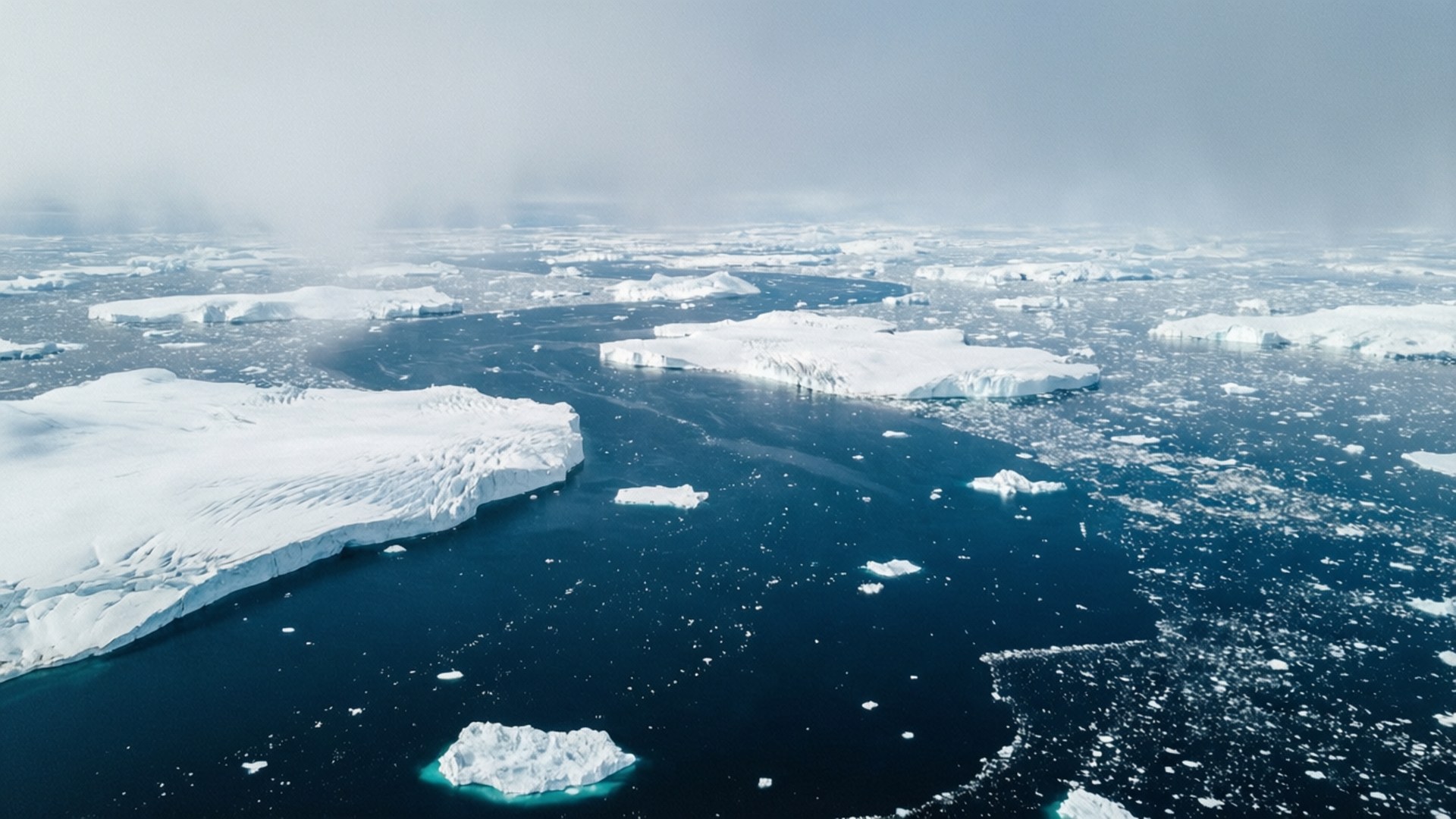 Arctic Ocean 桌布 壁紙 — 從高空俯瞰廣闊的北極海域，點綴著漂浮的冰山和浮冰，天空朦朧。