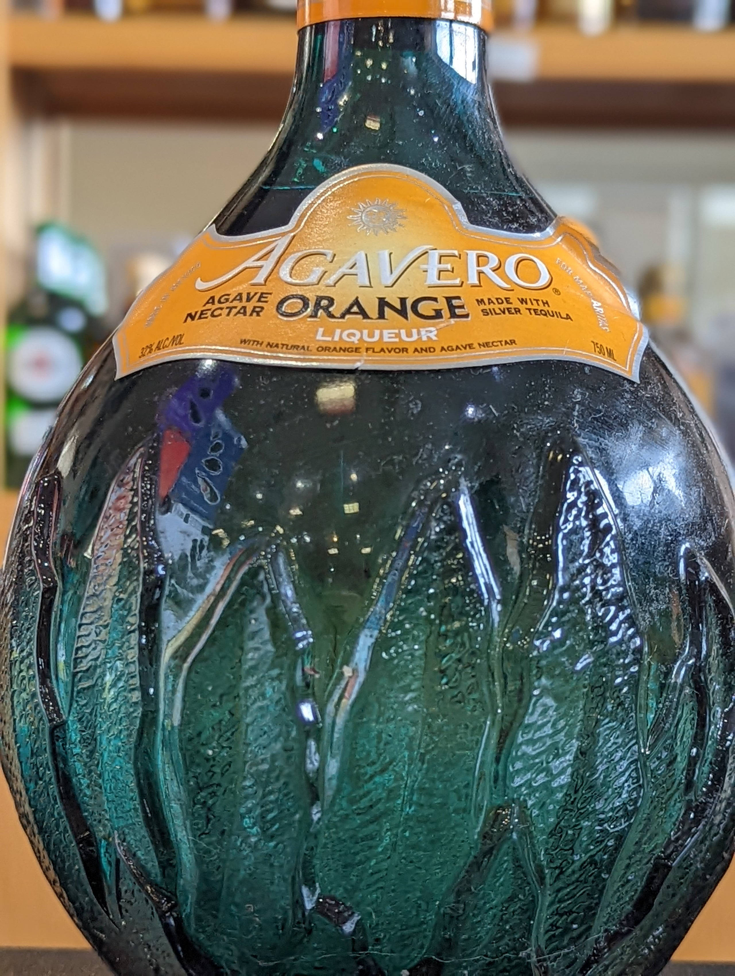 手機 桌布 壁紙 — Agavero Orange 利口酒的青綠色玻璃瓶特寫，表面有紋理和橙色標籤。