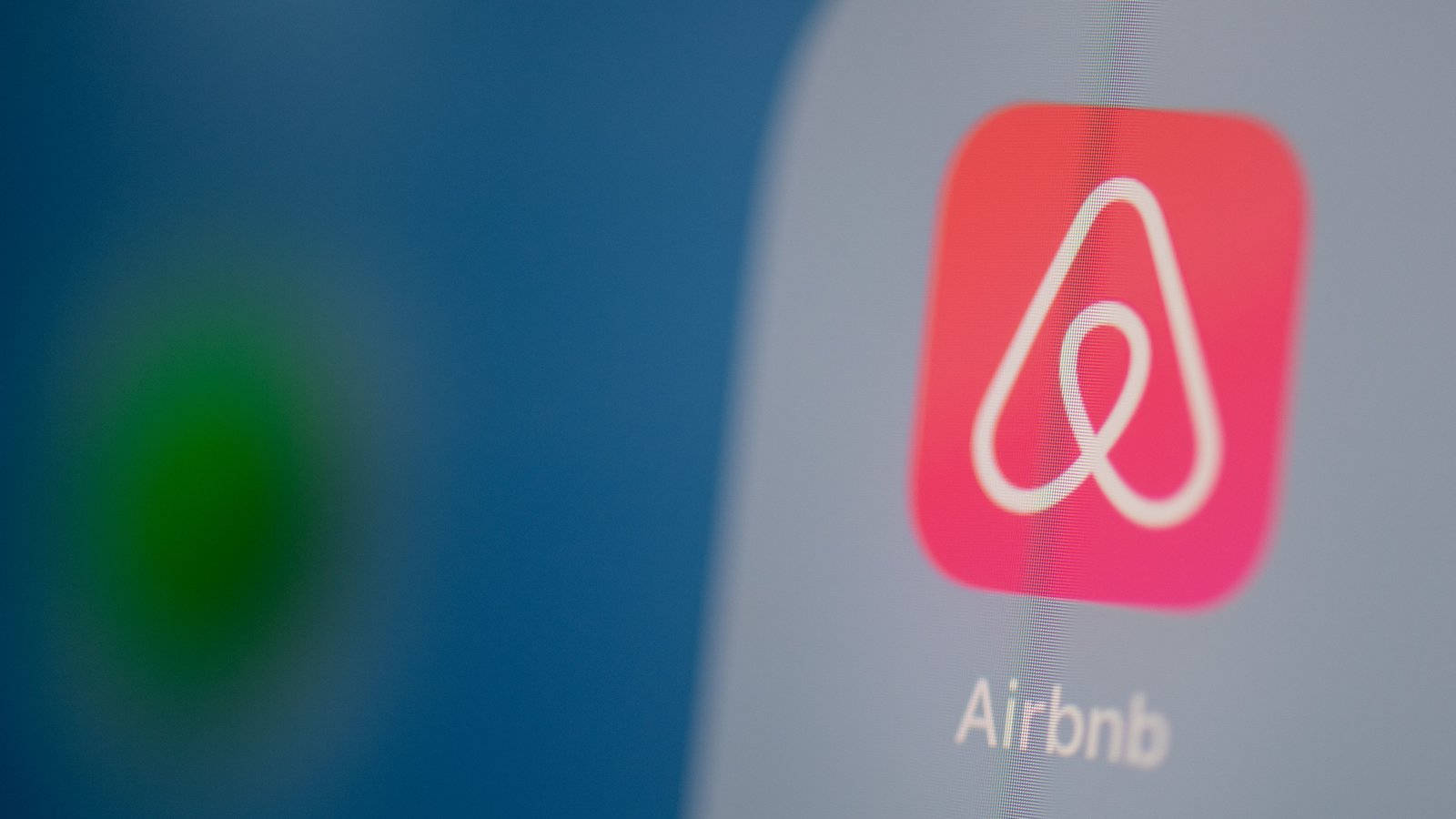 Application 桌布 壁紙 — Airbnb應用程式圖標在智慧型手機螢幕上發出粉紅色光芒的特寫，背景為模糊多彩。