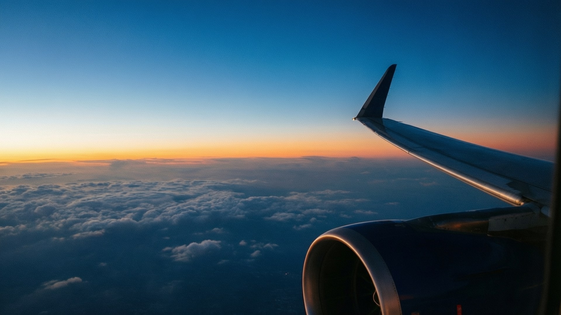Airplane Window Sky 壁紙 — 飛機機翼和引擎在日出時翱翔於雲海之上，天空由橙色漸變至深藍色。