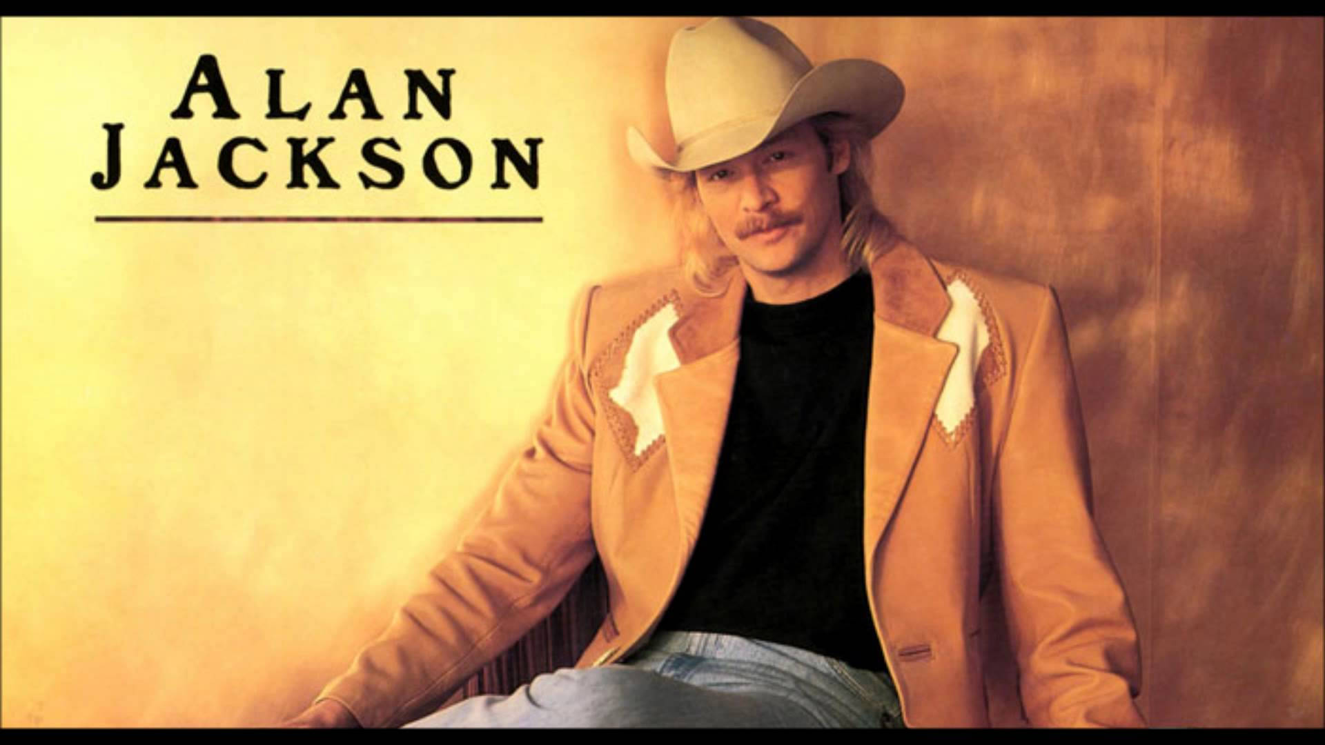 Alan Jackson 桌布 壁紙 — Alan Jackson 自信地戴著牛仔帽和棕褐色外套，站在溫暖的金色背景前。