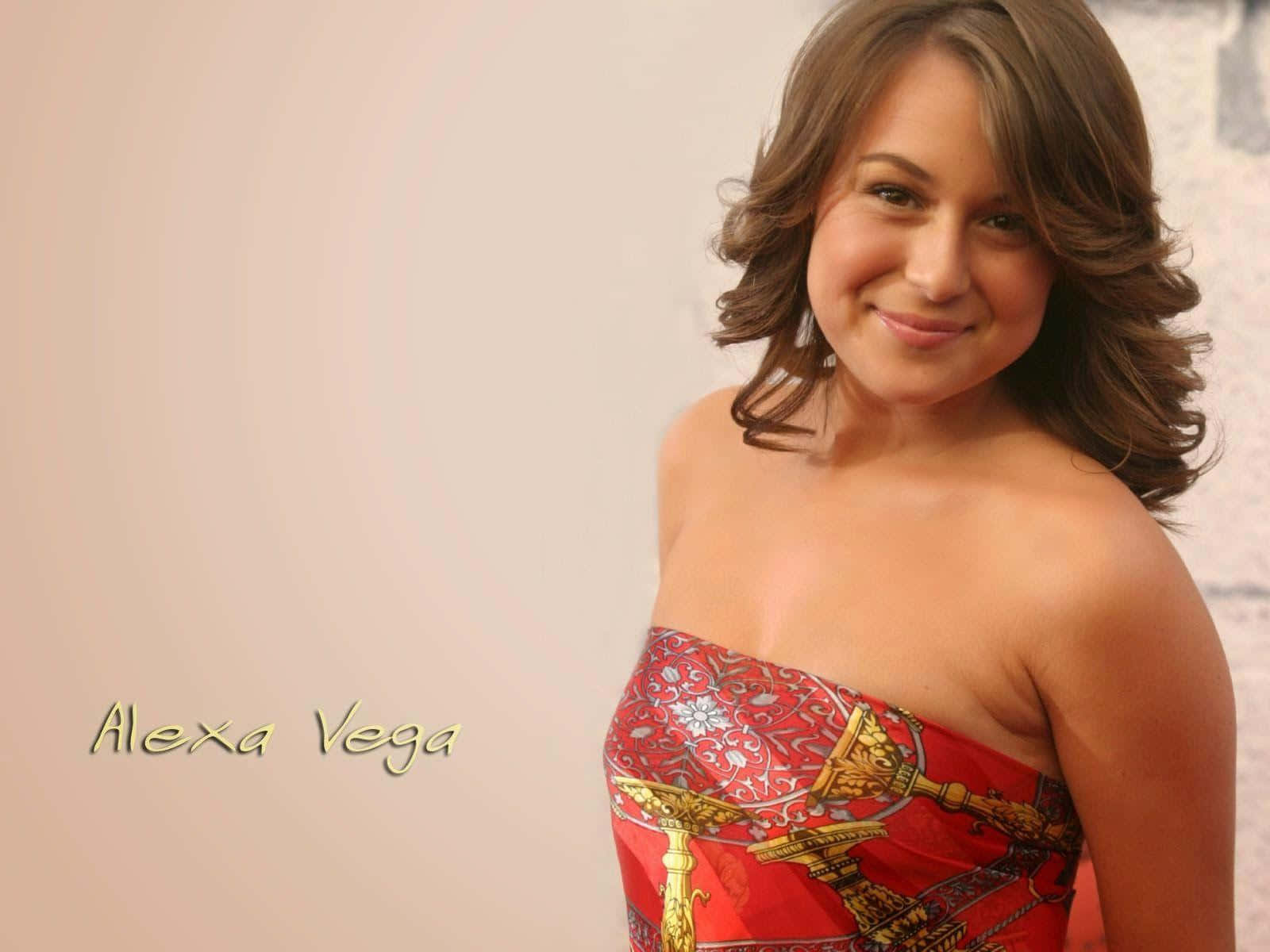 Alexa Penavega 桌布 壁紙 — Alexa Vega 在柔和米色背景前，穿著鮮豔紅色圖案的露肩連身裙，溫暖地微笑。