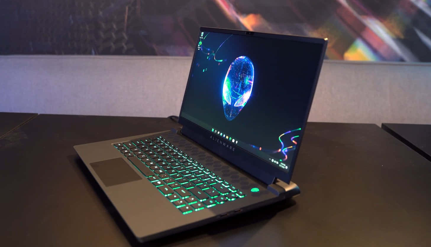 外星人 桌布 壁紙 — Alienware 筆記型電腦配備發光綠色鍵盤，在黑暗的桌子上打開，螢幕上顯示一個充滿活力的藍色全息球體。