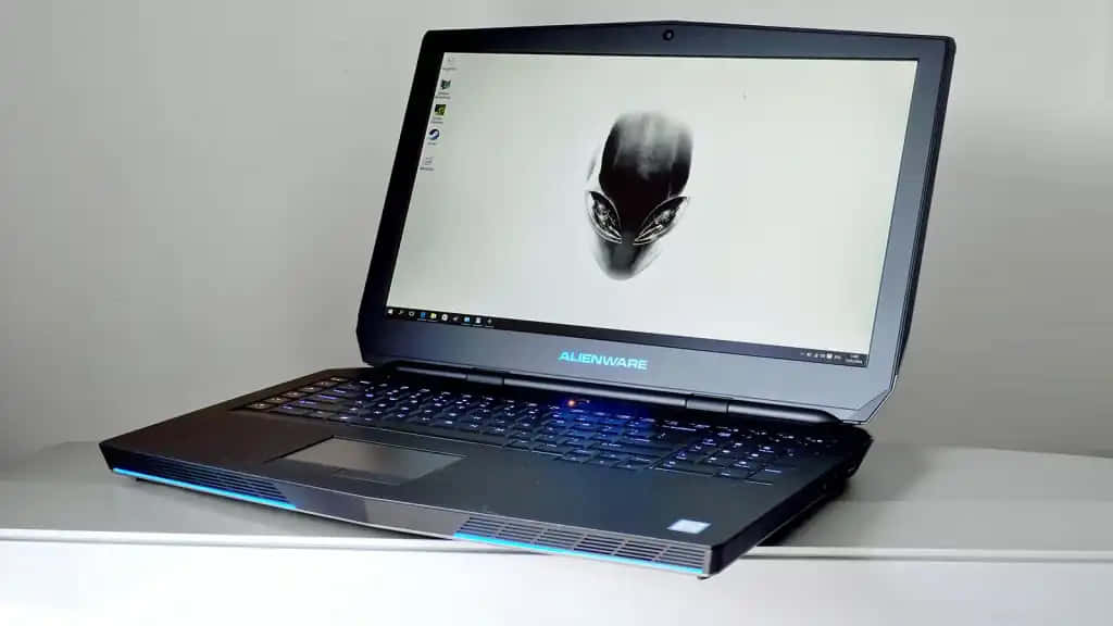 外星人 桌布 壁紙 — Alienware 遊戲筆記型電腦，帶有發光藍色鍵盤和螢幕上外星人標誌，打開放在白色表面上。
