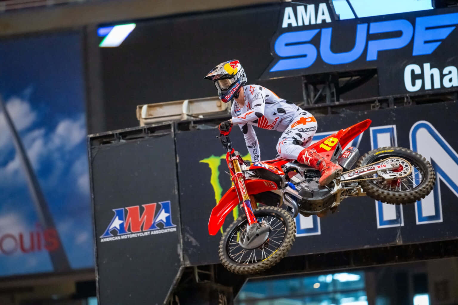  壁紙 — AMA Supercross Championship 賽事中，紅色越野摩托車車手在體育館跳台上凌空飛翔。