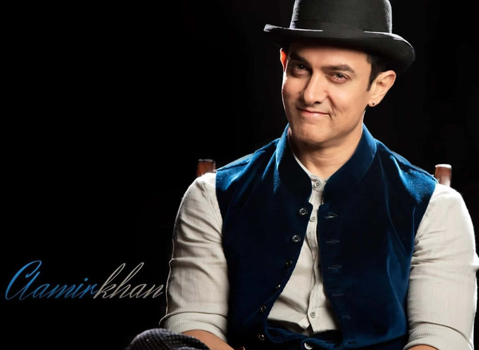 Aamir Khan 桌布 壁紙 — Aman Khan 戴著黑色圓頂禮帽和藍色天鵝絨背心，在純黑背景下自信微笑。