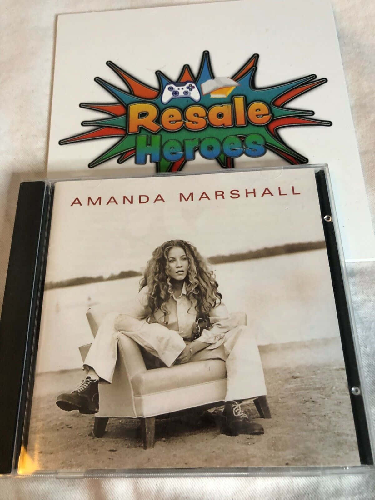 Marshall 桌布 壁紙 — Amanda Marshall 的棕褐色調 CD 封面顯示她坐在沙灘的椅子上，上方有一個「Resale Heroes」貼紙。