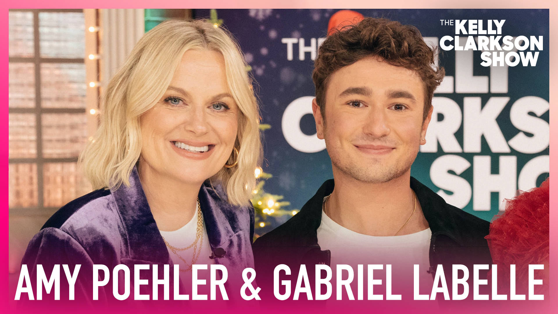 女演員 桌布 壁紙 — Amy Poehler 和 Gabriel Léveille 在一個燈光明亮的脫口秀場景中溫暖地微笑，周圍有節日燈光和粉紅色邊框。