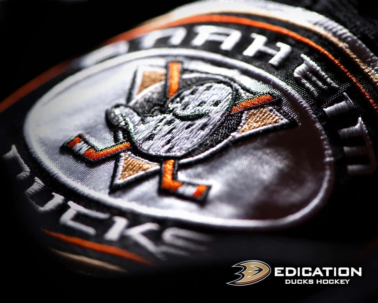 安納海姆鴨隊 桌布 壁紙 — Anaheim Ducks 冰球隊刺繡徽章的近距離特寫，在深色布料上呈現細緻縫線和金屬光澤。