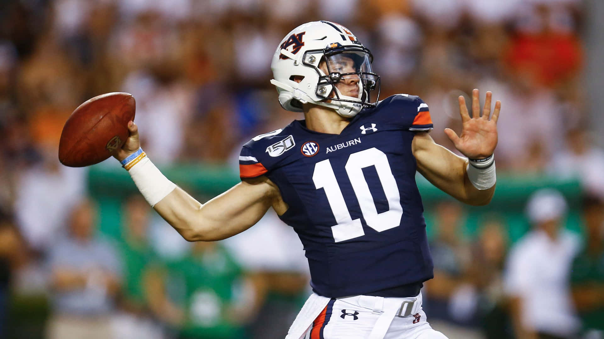  壁紙 — 奧本大學美式足球四分衛10號身穿海軍藍球衣，在體育館燈光下準備在比賽中傳球。