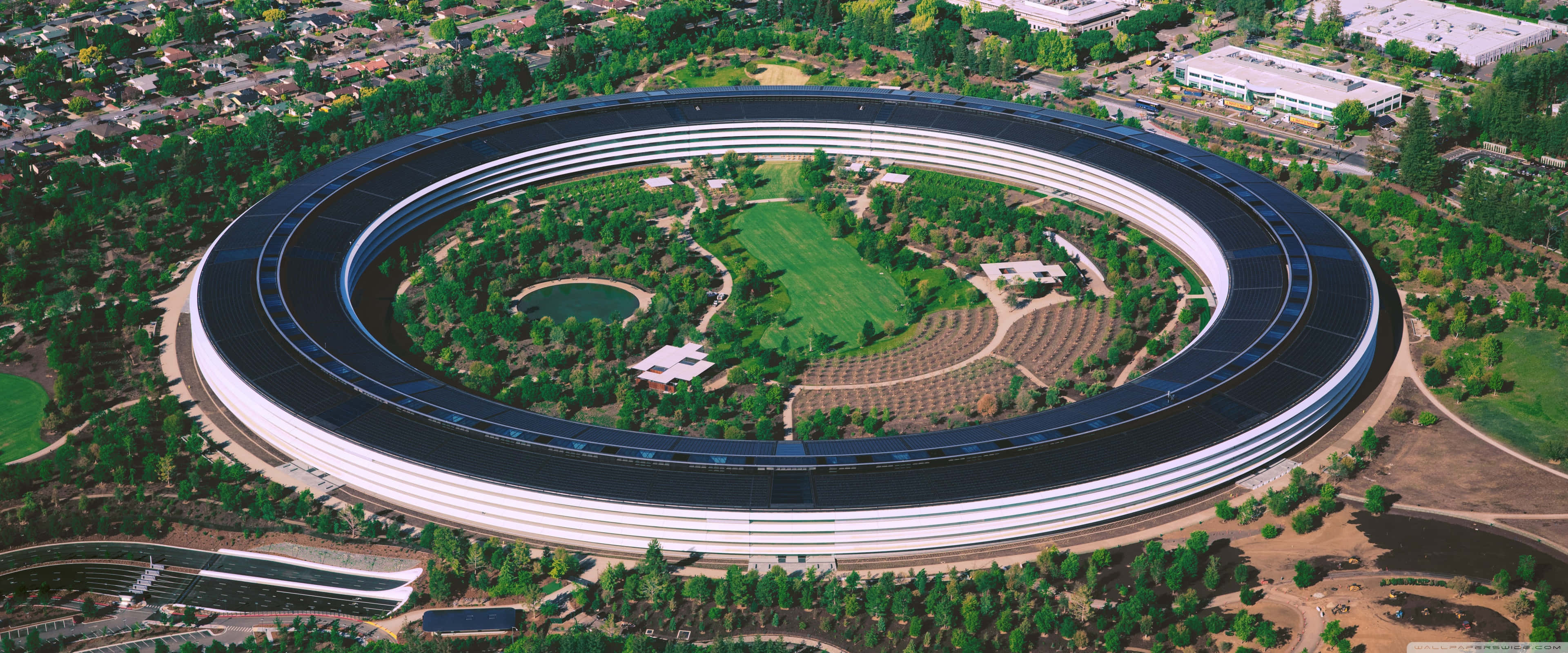 Apple 3840x1600 桌布 壁紙 — Apple Park 標誌性圓形太空船建築的鳥瞰圖，周圍環繞著茂密的綠化和修剪整齊的草坪。