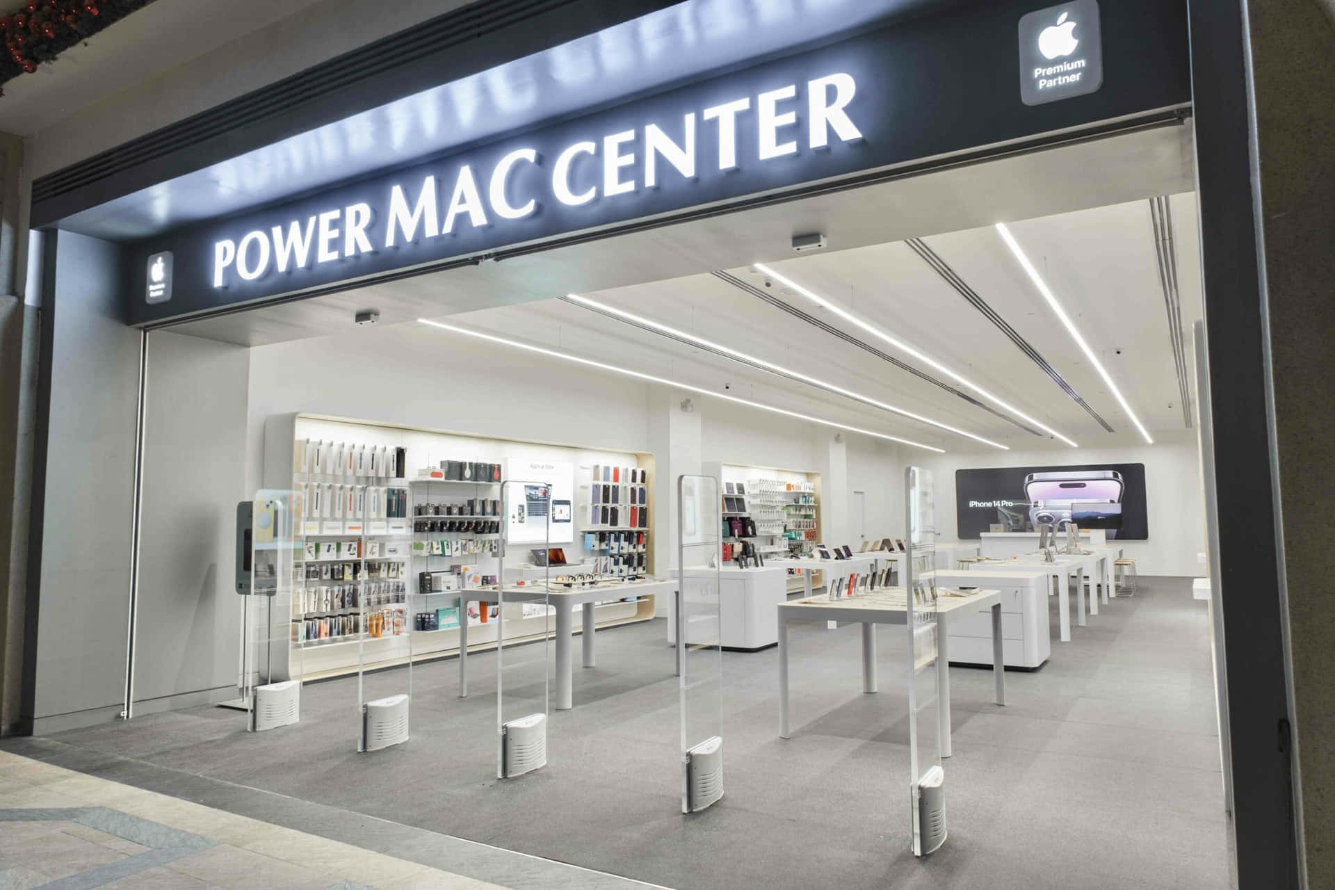 Apple 商店入口，帶有 'Power Mac Center' 標誌和白色展示桌。 — Macbook Pro 壁紙