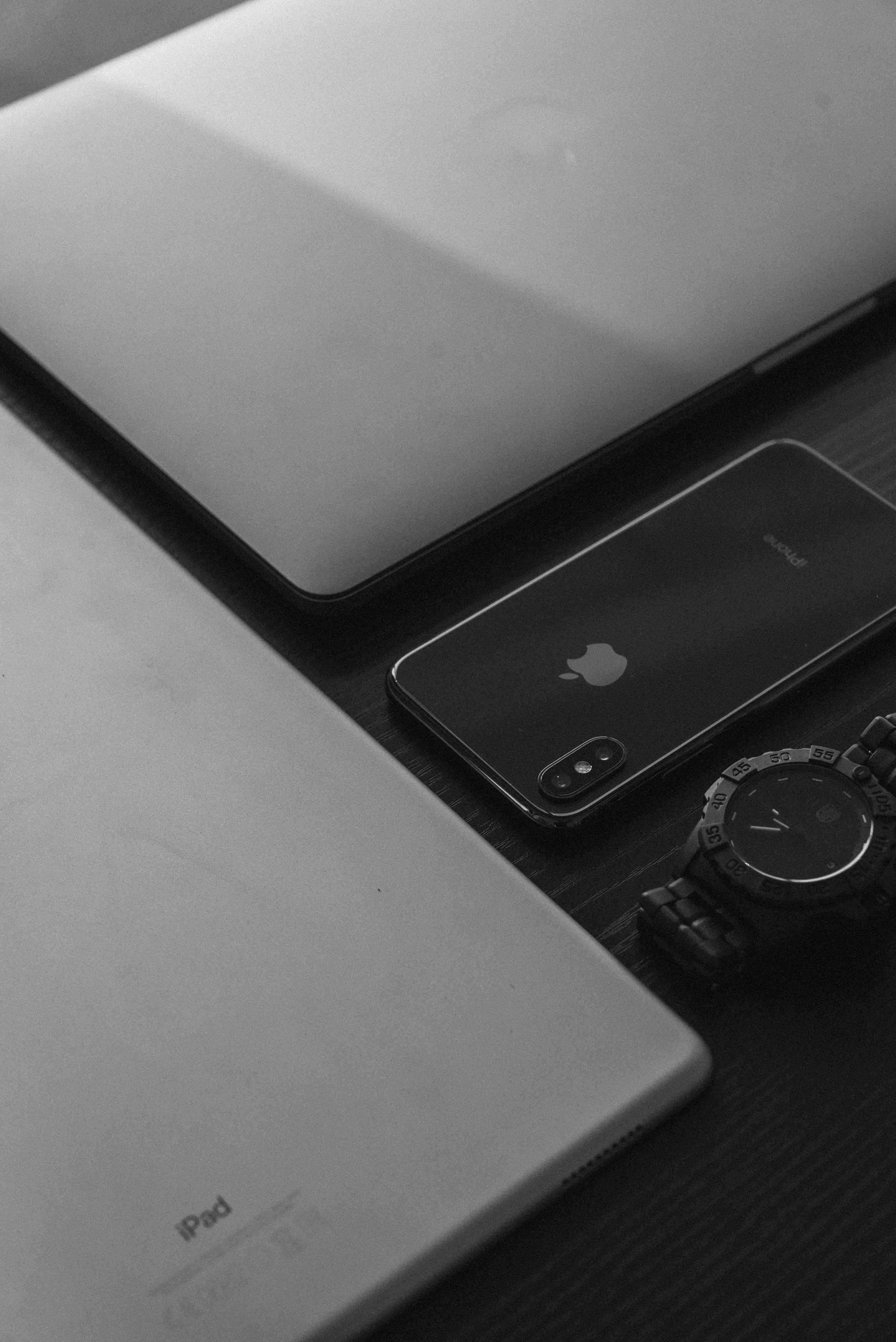 minimal dark iPhone 桌布 壁紙 — Apple 裝置和堅固手錶在深色木質表面上的單色特寫。