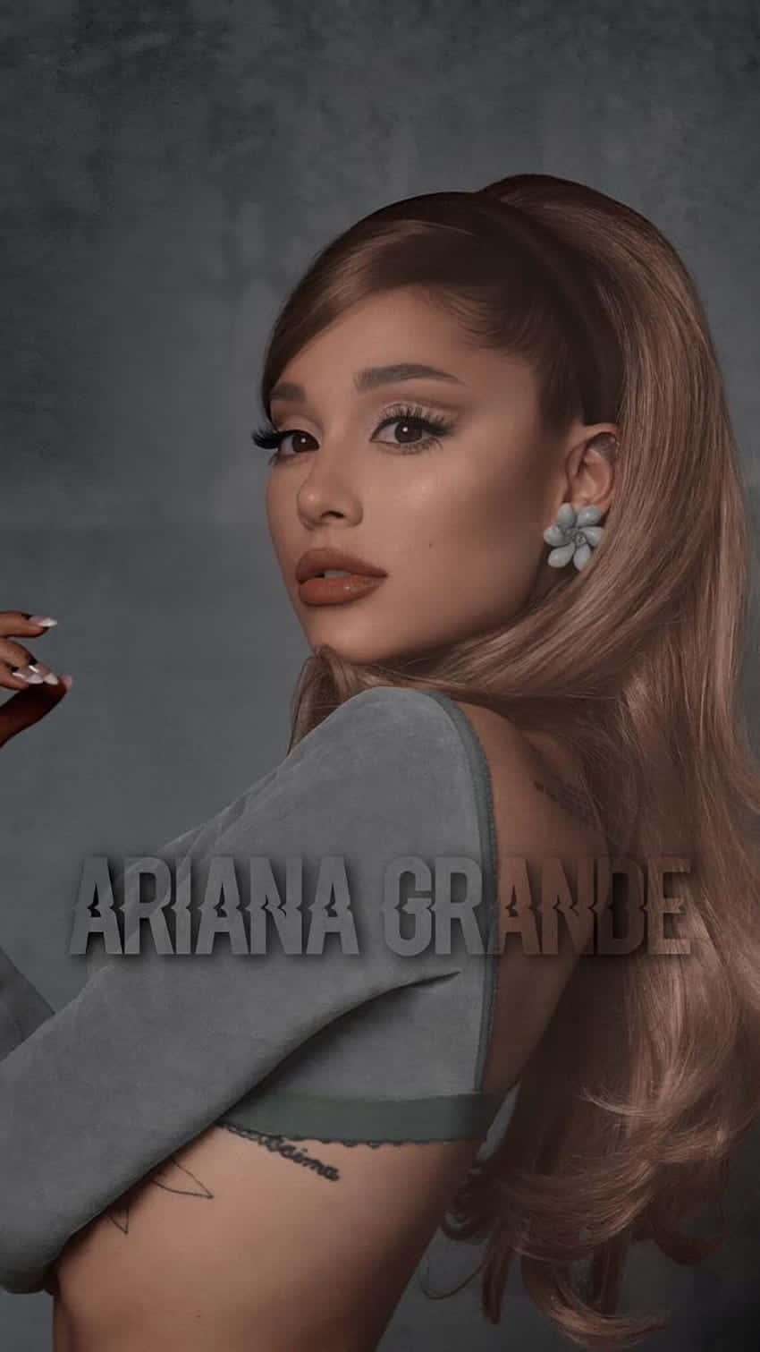  壁紙 — Ariana Grande 穿著灰色上衣，在帶有紋理的灰色背景前擺姿勢，戴著花朵耳環，露出刺青。