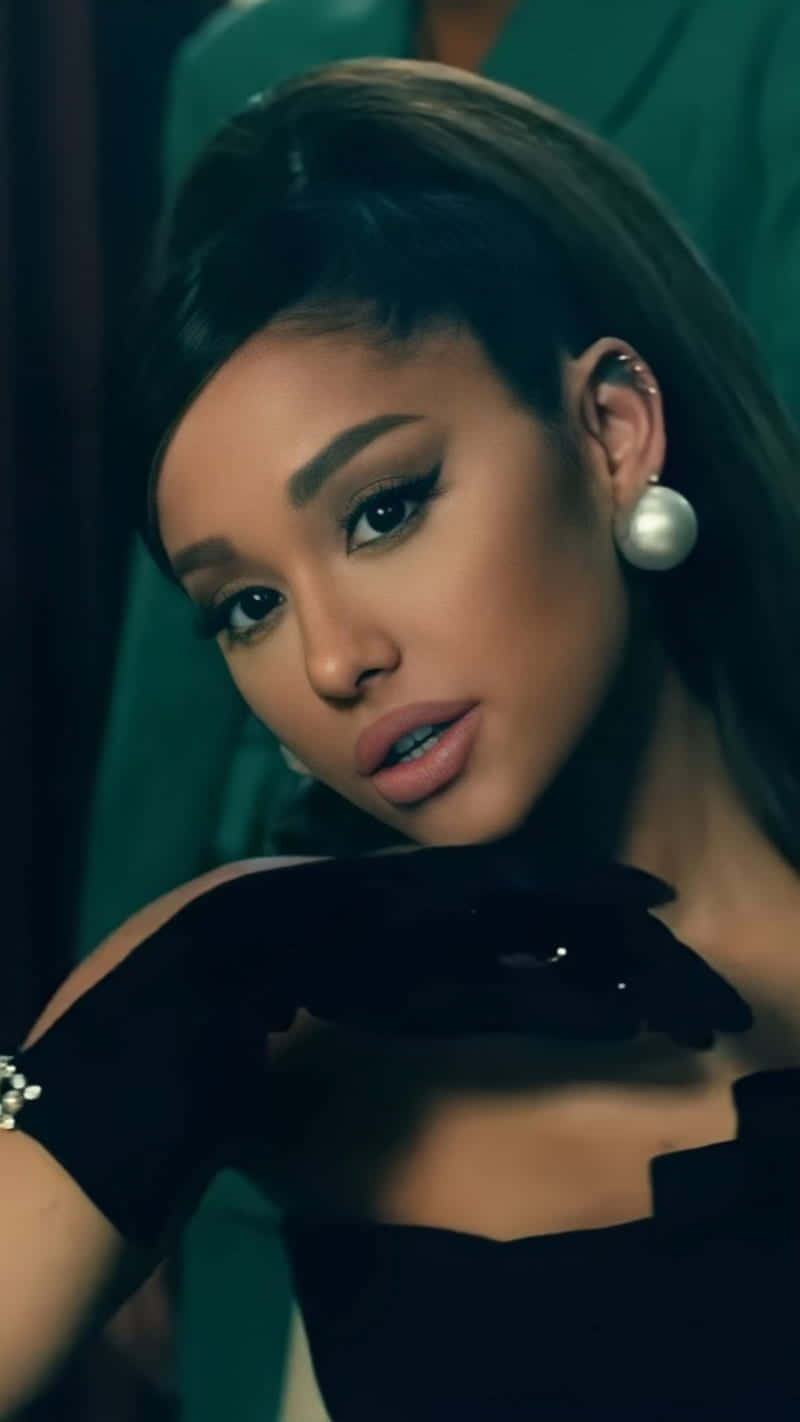  壁紙 — Ariana Grande 在昏暗的房間中，戴著黑色手套和珍珠耳環，對著青綠色背景凝視。