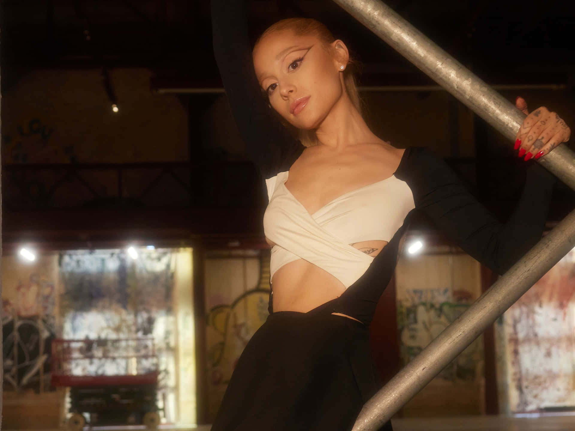  壁紙 — Ariana Grande 在溫暖燈光下，於佈滿塗鴉的都市背景前，自信地擺出黑白造型。
