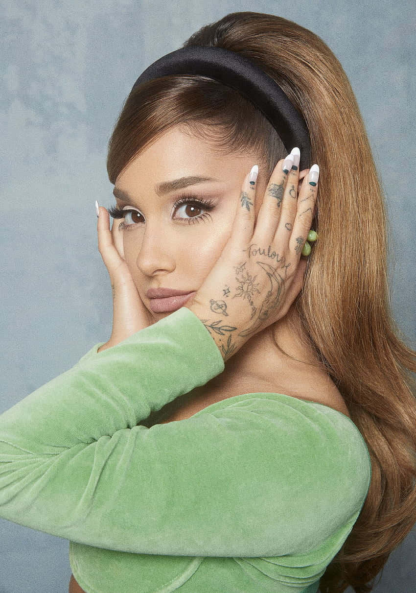 壁紙 — Ariana Grande 將手放在臉旁，身穿綠色天鵝絨上衣和黑色頭帶，背景為有紋理的藍色。