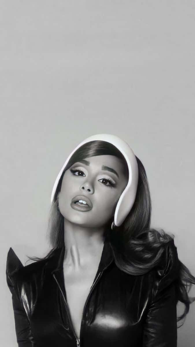  壁紙 — Ariana Grande 身穿黑色皮夾克和白色頭飾，在純灰色背景前擺出引人注目的單色肖像。