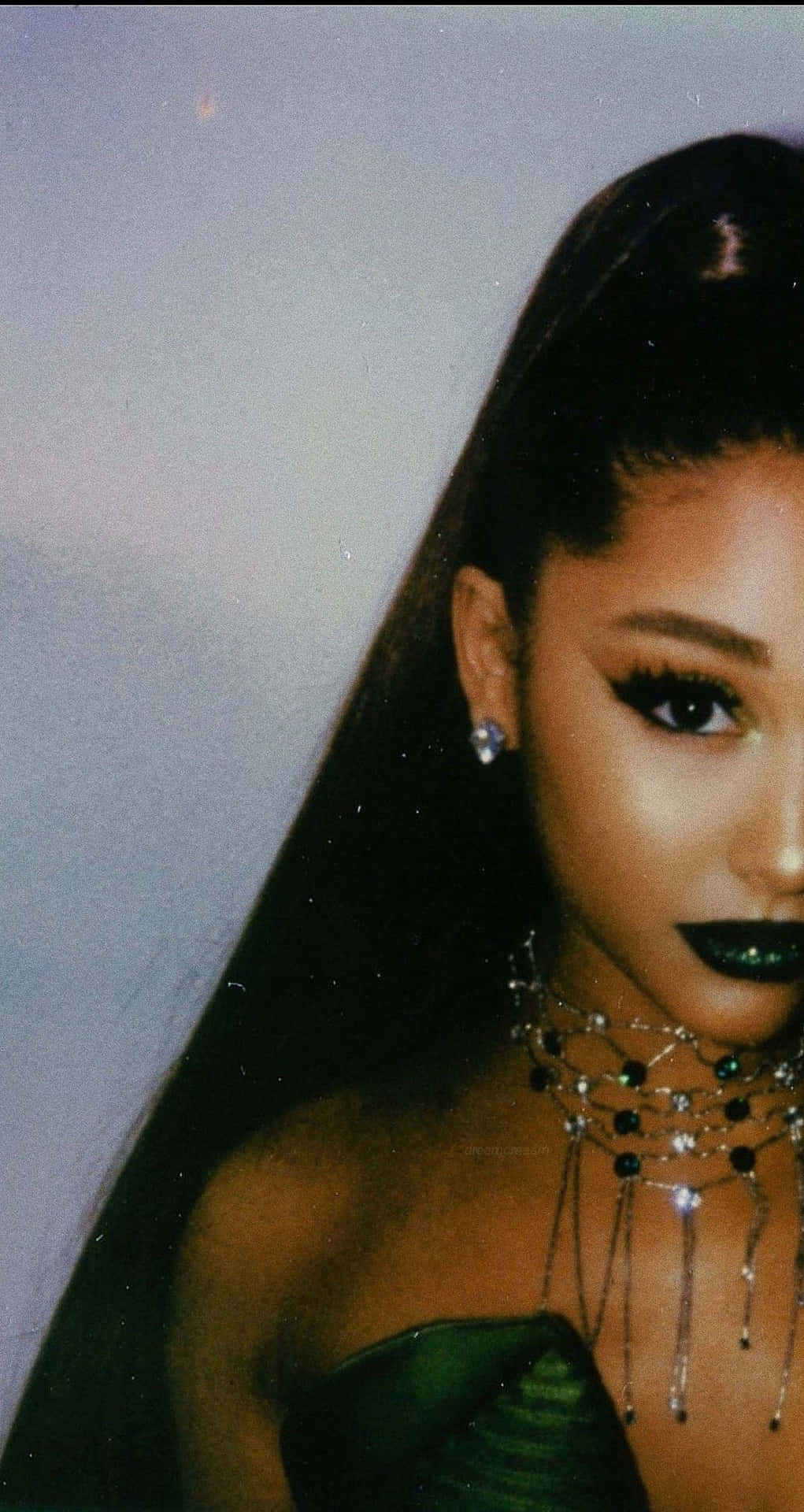  壁紙 — Ariana Grande 身穿華麗綠色服裝，搭配大膽妝容和閃亮珠寶，背景為柔和灰色。