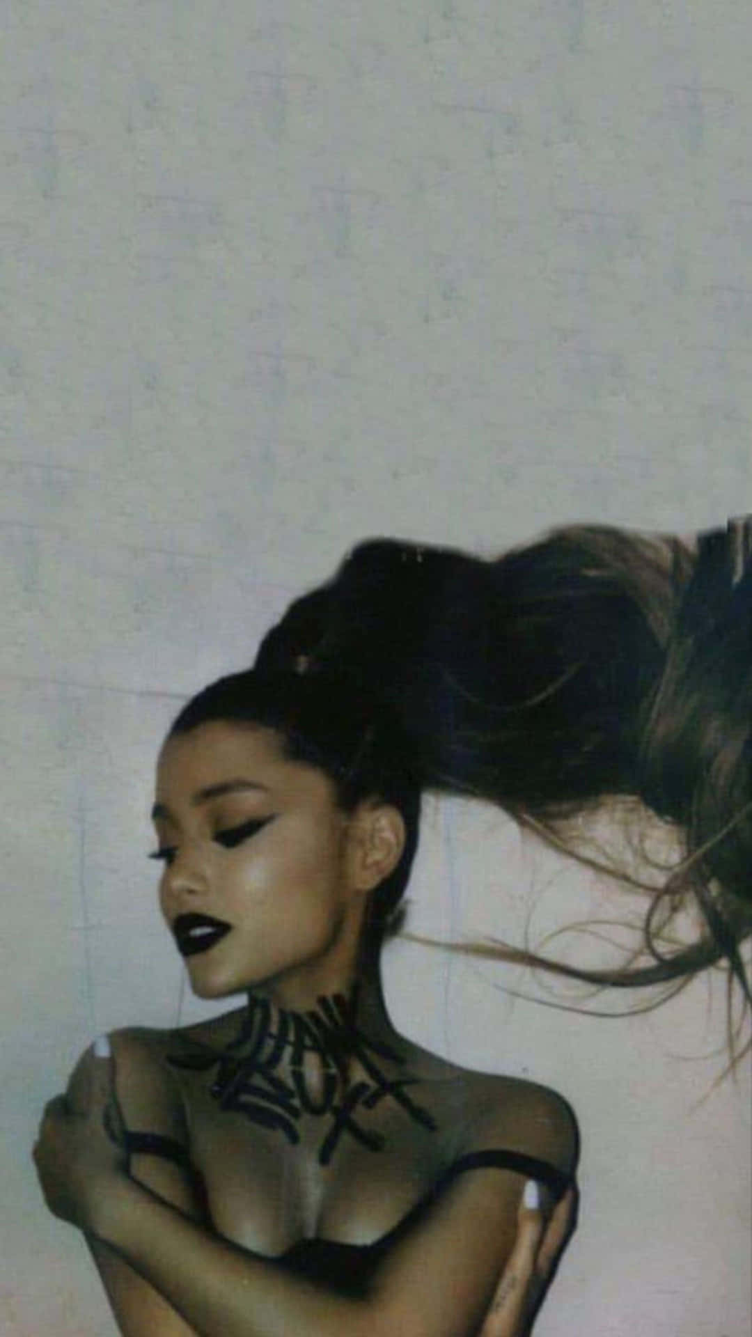  壁紙 — Ariana Grande 塗上深色唇膏，頸部和肩膀有黑色標記，背景是素牆。