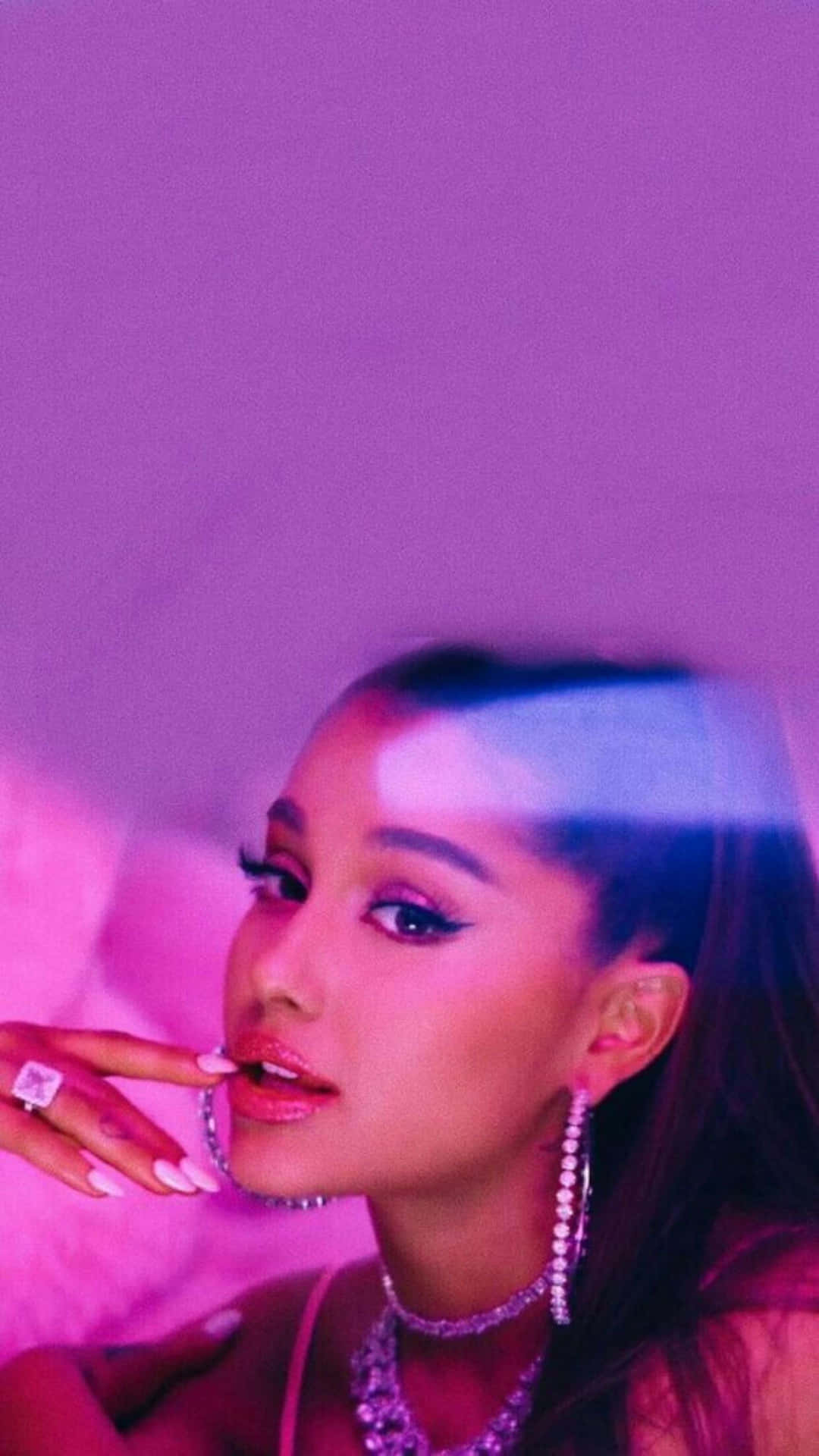  壁紙 — Ariana Grande 在充滿活力的紫色迷霧中迷人地擺姿勢，飾以閃閃發光的珠寶和濃妝。