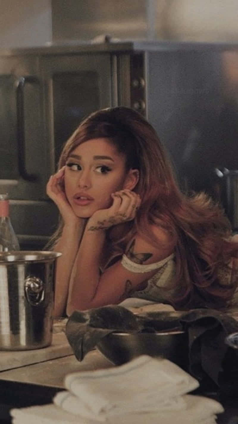  壁紙 — Ariana Grande 在光線昏暗的廚房裡，用不鏽鋼電器和白色毛巾，將下巴擱在手上。