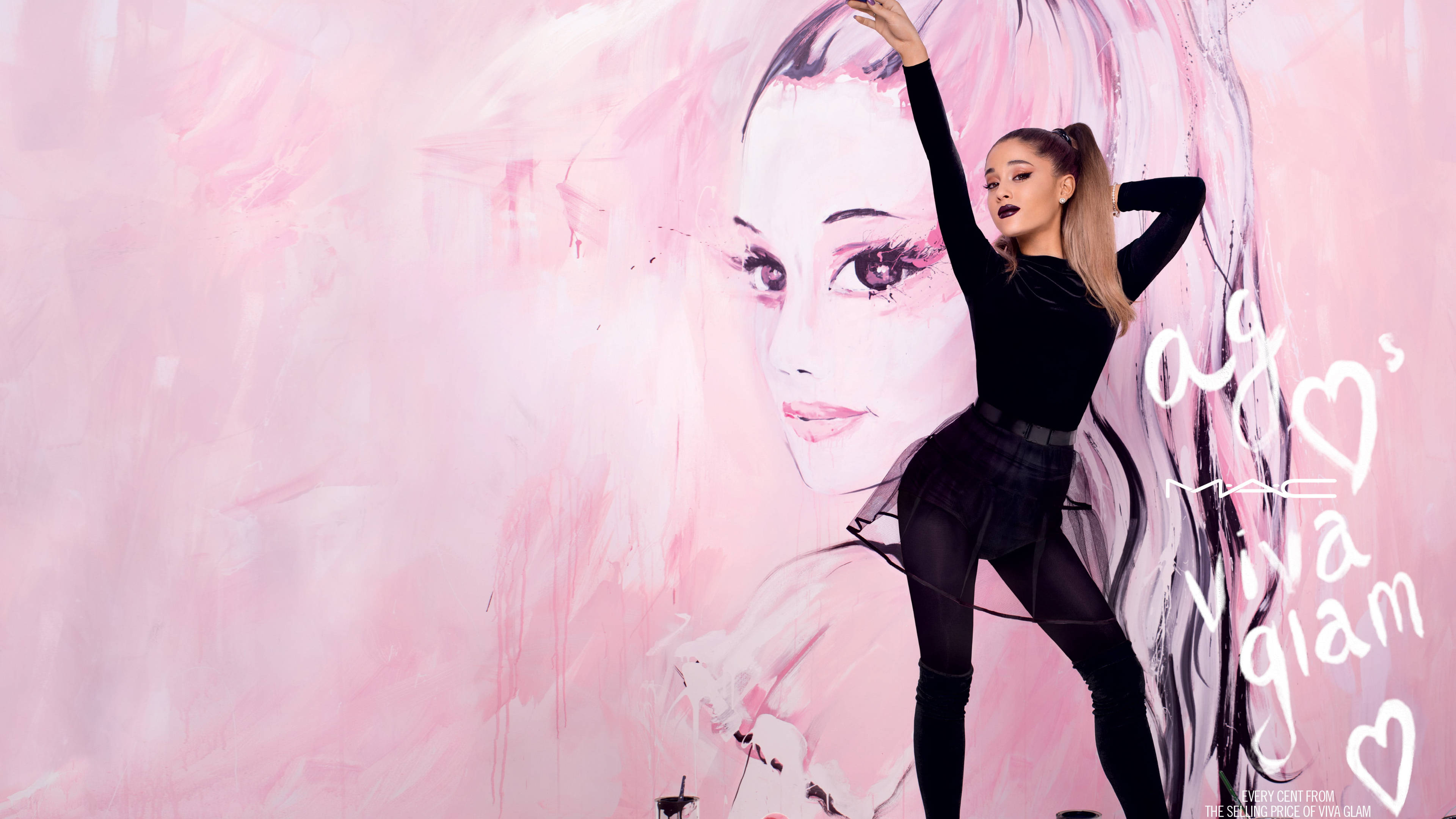 Cosmetics 桌布 壁紙 — Ariana Grande 在一個大型粉紅色壁畫前動態擺姿勢，壁畫上是她的臉，帶有MAC Viva Glam品牌標誌。