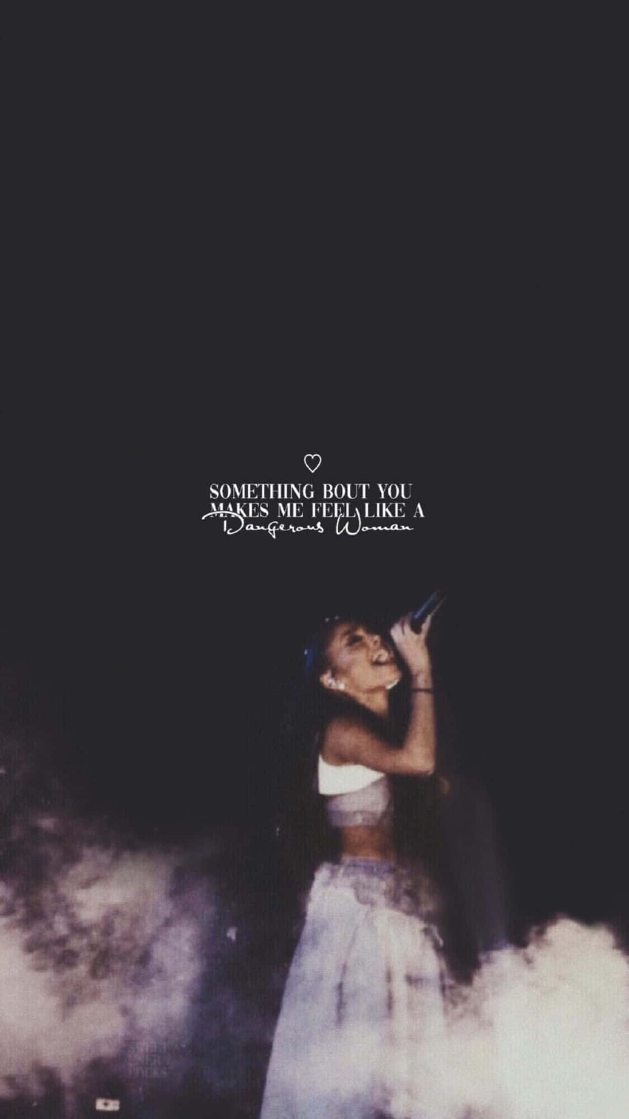 Aesthetic Ariana Grande 桌布 壁紙 — Ariana Grande 在夜晚煙霧瀰漫的舞台上表演，燈光戲劇化，她上方有文字 'Something Bout You Makes Me Feel Like A Dangerous Woman'。