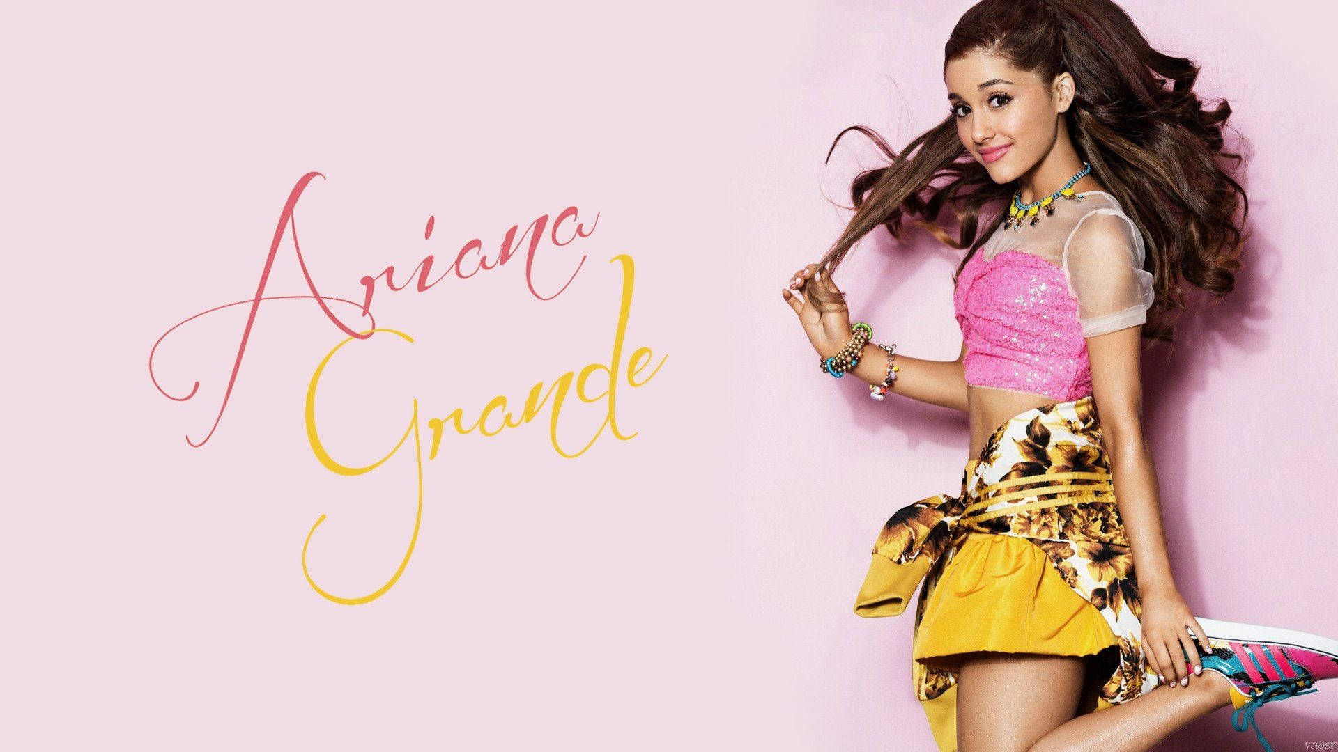 Grande 桌布 壁紙 — Ariana Grande 在柔和的粉紅色背景前頑皮地擺姿勢，她的名字以優雅的草書字體呈現。