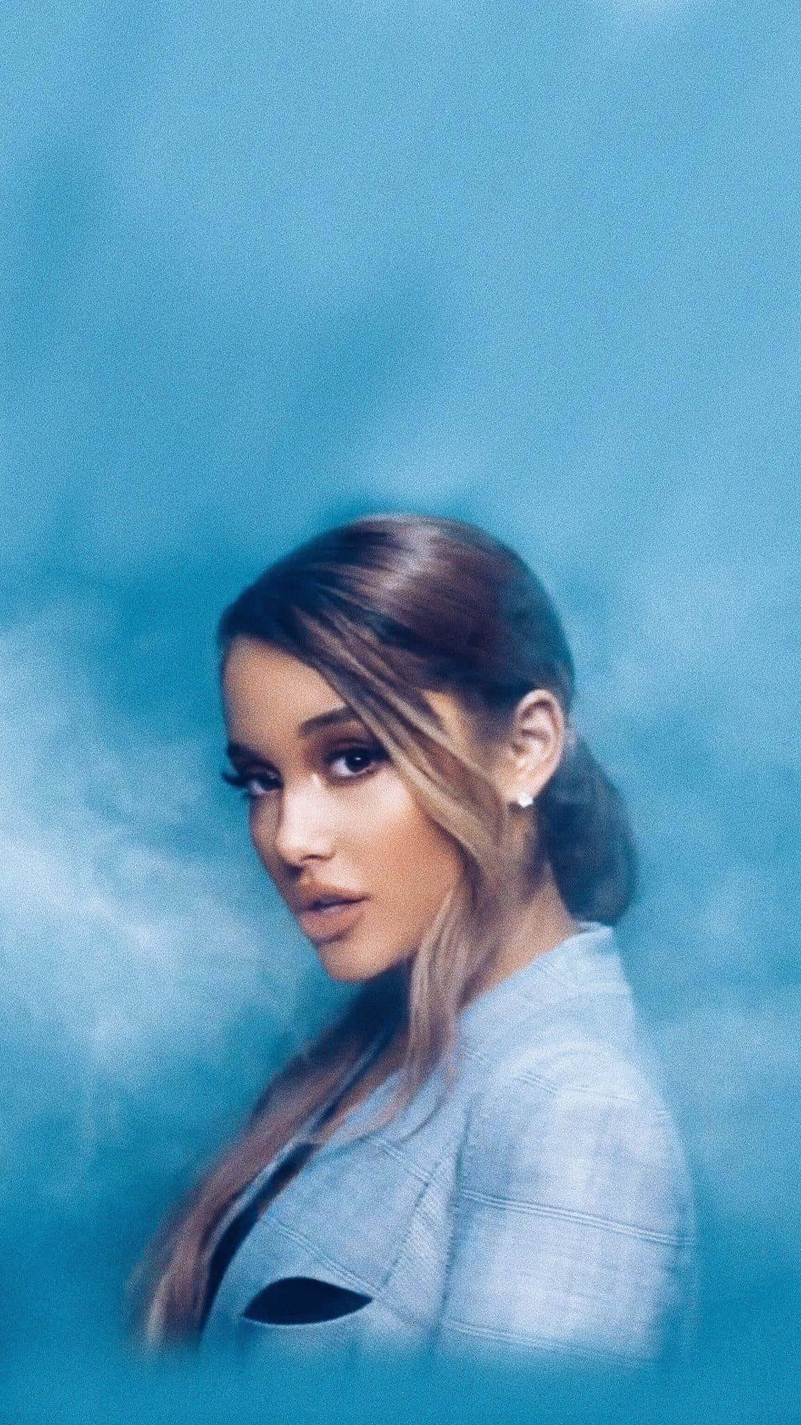 Aesthetic Ariana Grande 桌布 壁紙 — Ariana Grande 在煙霧瀰漫的氛圍燈光下，溫柔地凝視著模糊的藍色背景。