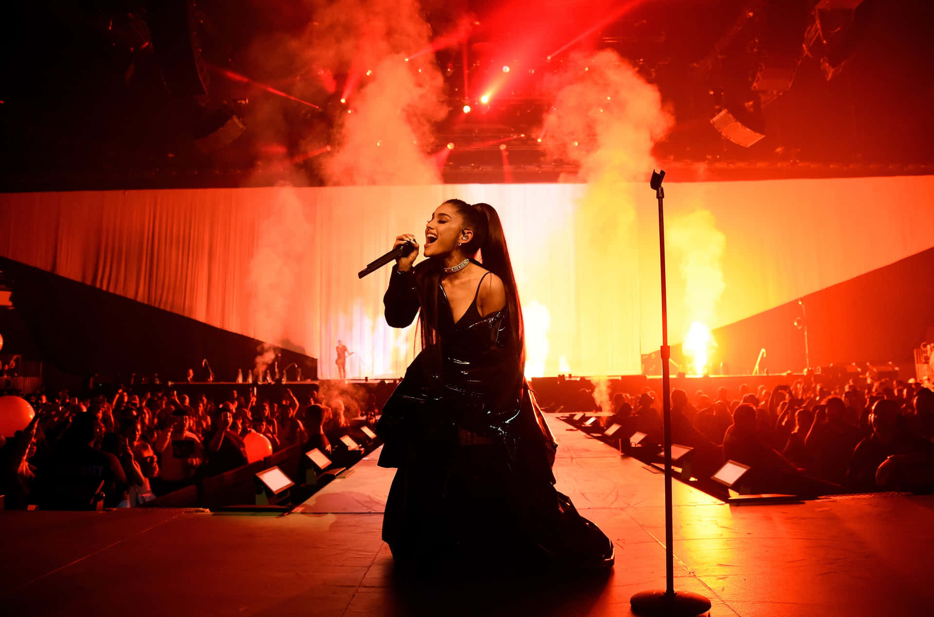 Ariana Grande 在紅色燈光的舞台上唱歌，伴有煙霧和人群。 — 亞莉安娜·格蘭德 GIF 壁紙